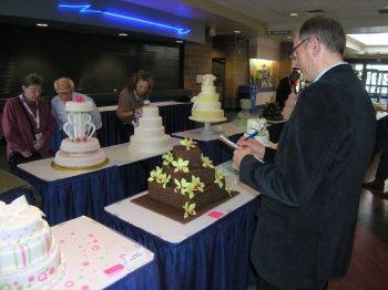 A judge scrutinizes an entry in the wedding cake competition while spectators look on.